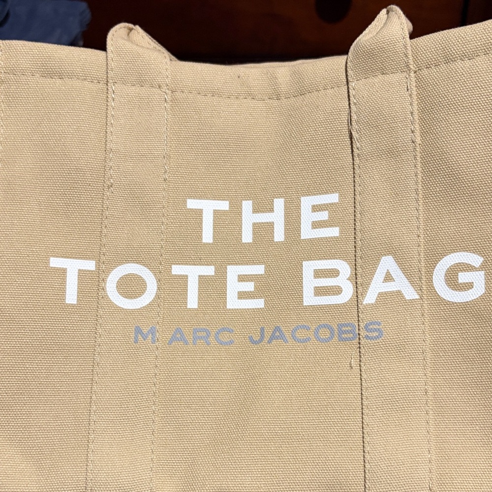 Marc Jacobs Beige Canvas Tote with White Logo with a crossbody strap.
